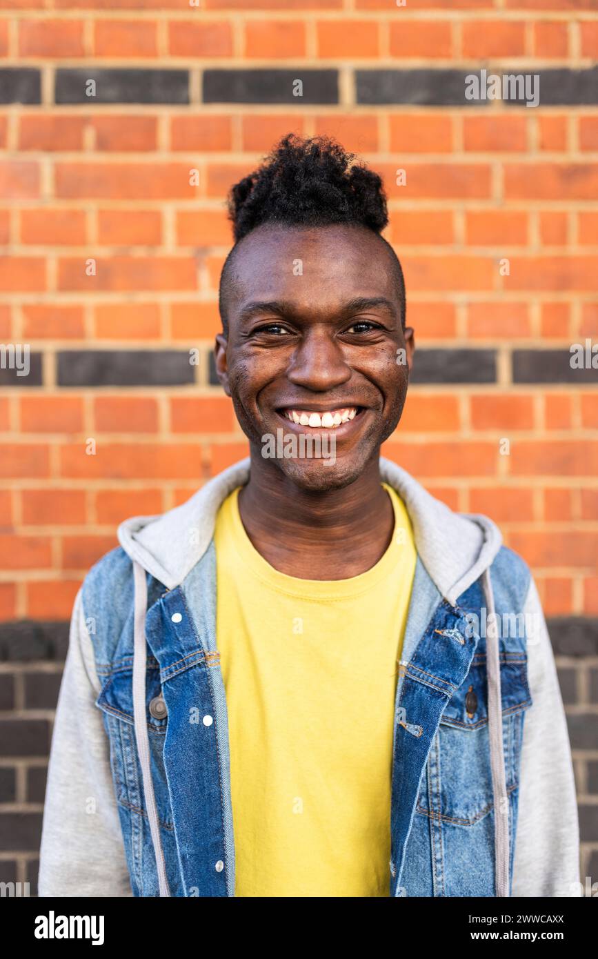 Smiling young man standing in front of brick wall Stock Photo - Alamy