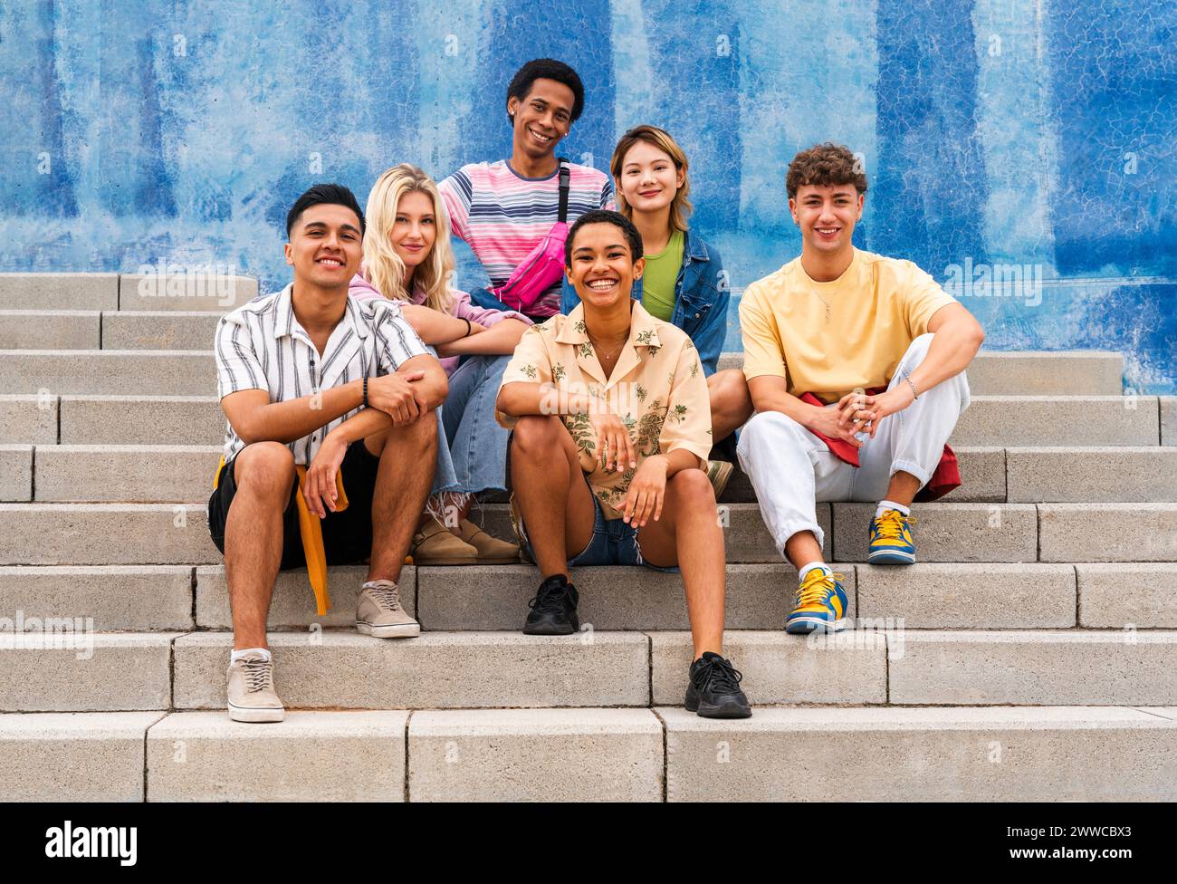 Multi ethnic group of young people sitting on steps in front of wall ...