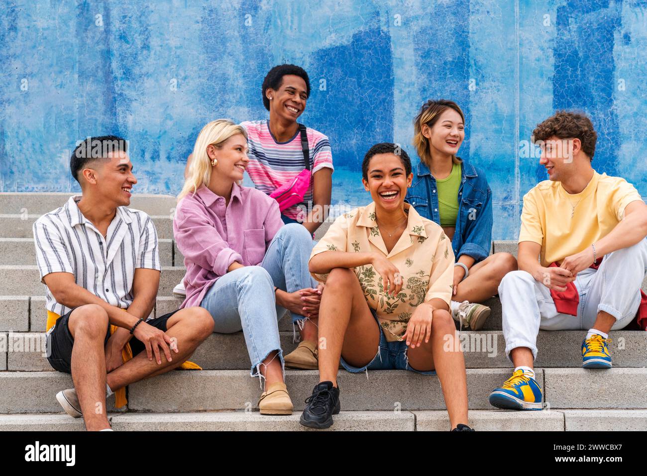 Multi ethnic group of young people sitting on steps in front of wall ...
