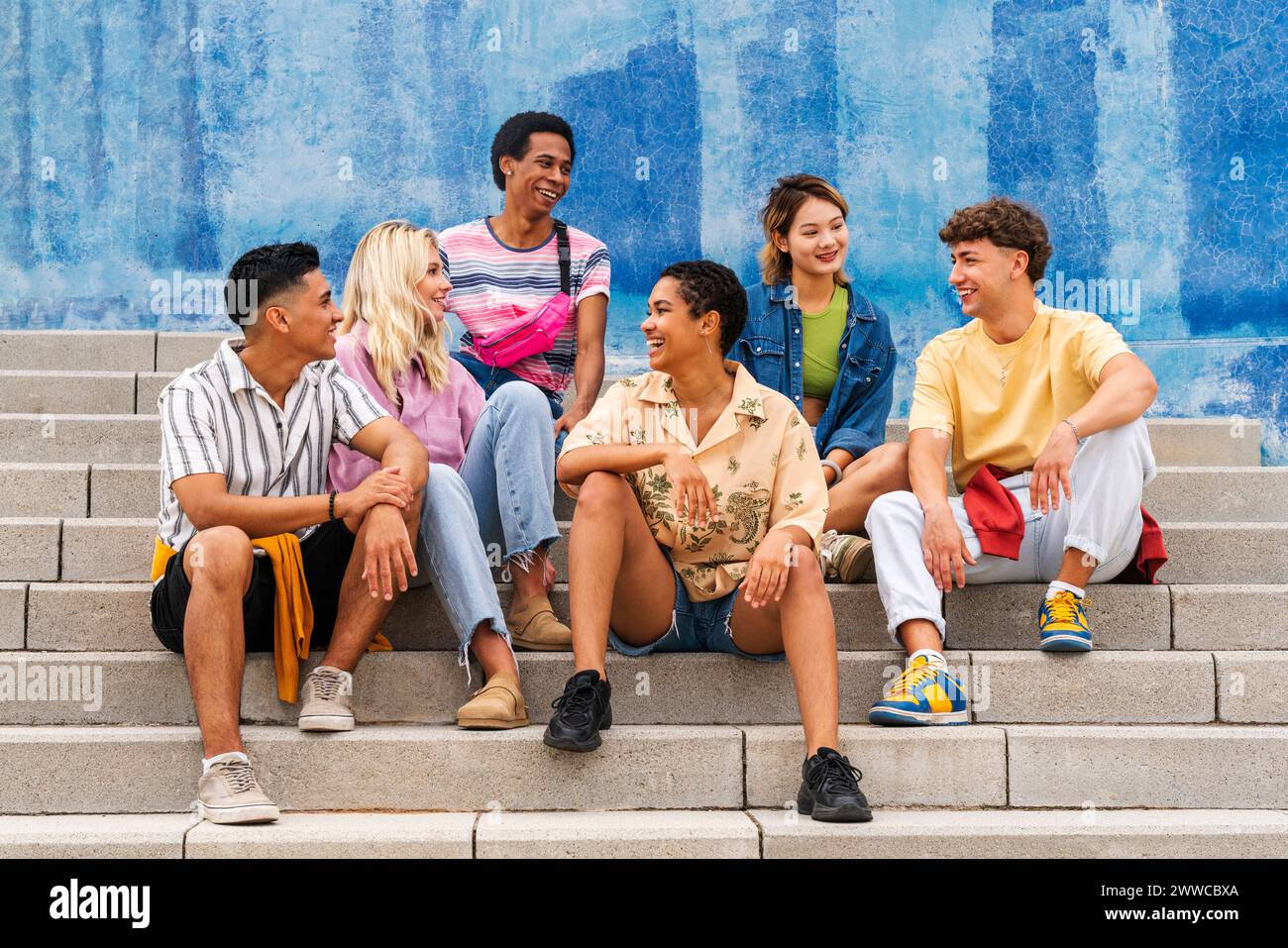 Multi ethnic group of young people sitting on steps in front of wall ...