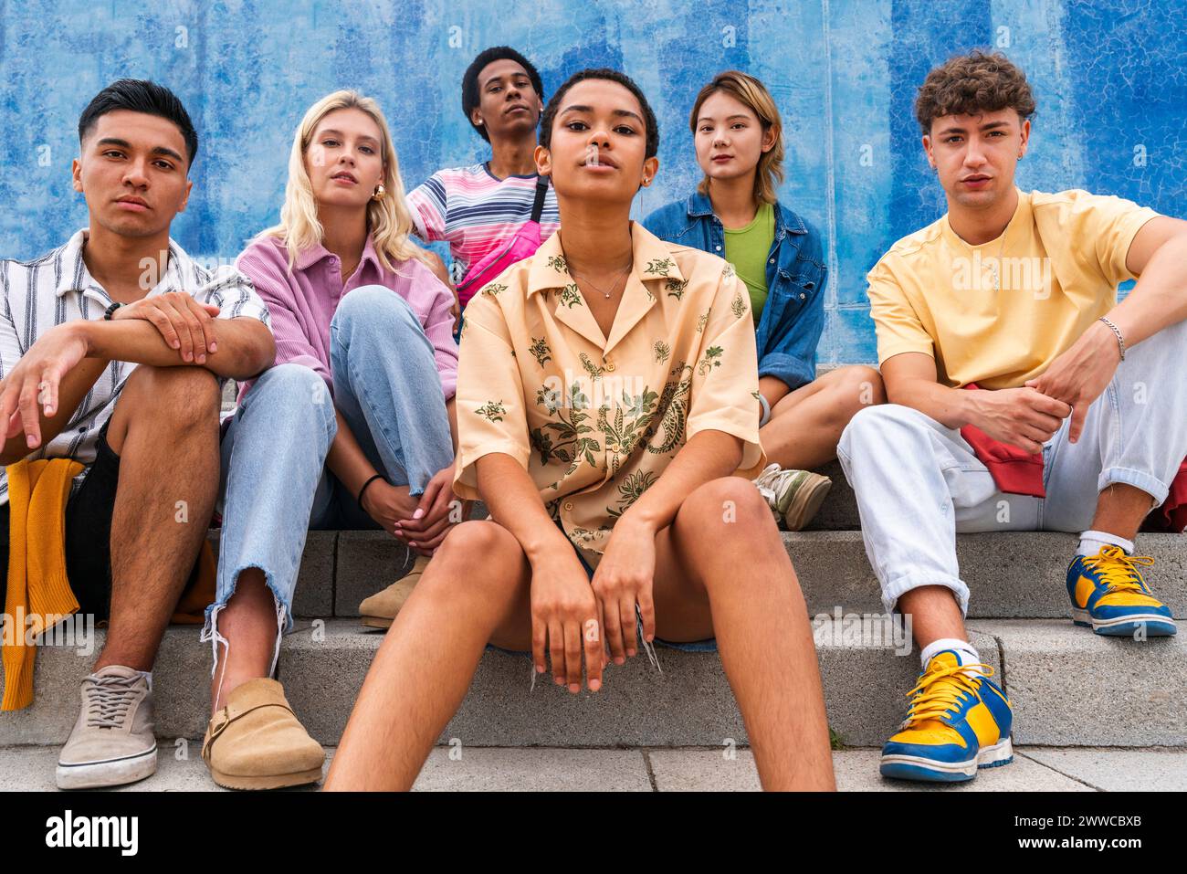 Confident young people sitting on steps in front of wall Stock Photo