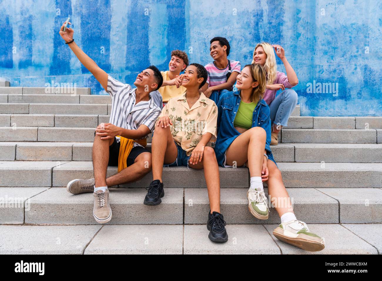 Happy group of young people taking selfie on steps in front of wall Stock Photo