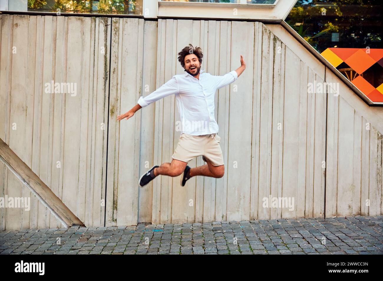Happy young man jumping in front of wall Stock Photo