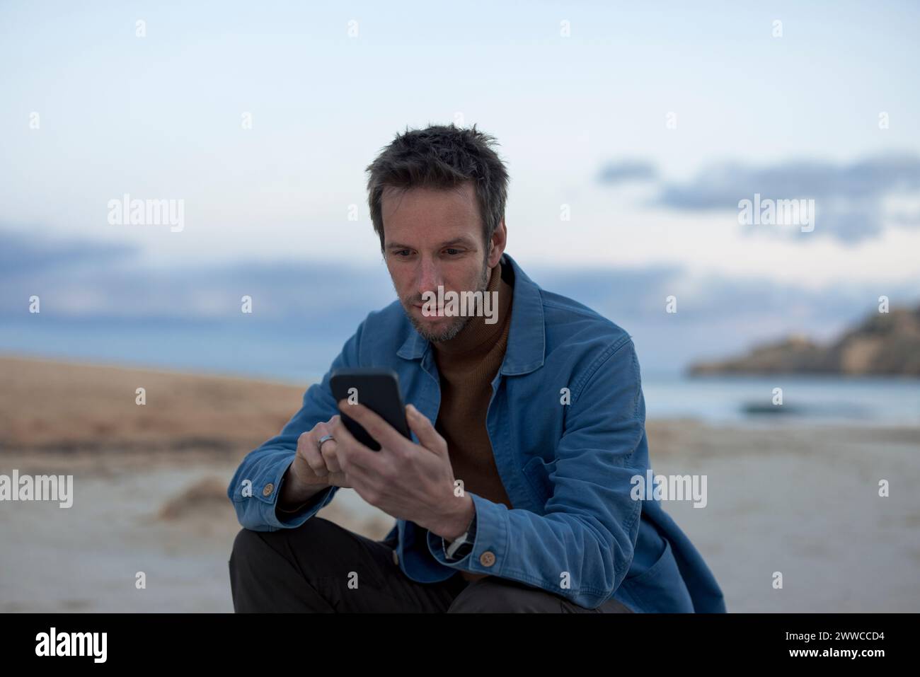 Man using smart phone at sunset beach Stock Photo
