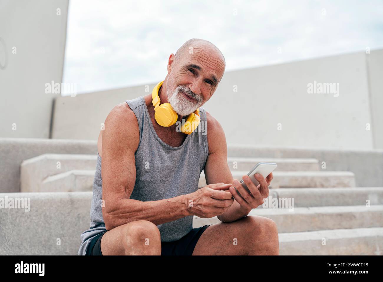 Smiling retired senior man using smart phone sitting on staircase Stock Photo
