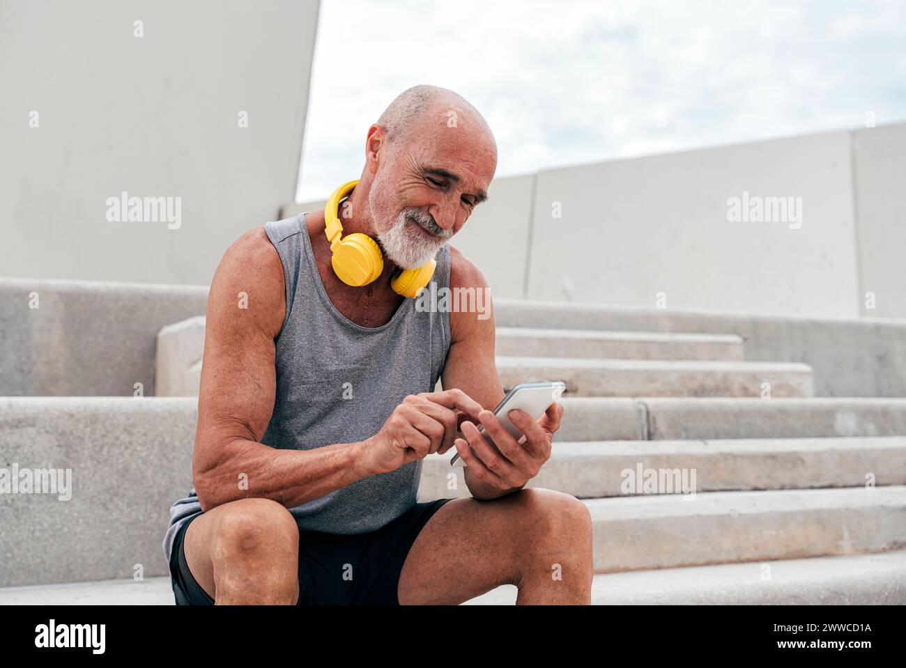 Smiling senior man using smart phone sitting on staircase Stock Photo