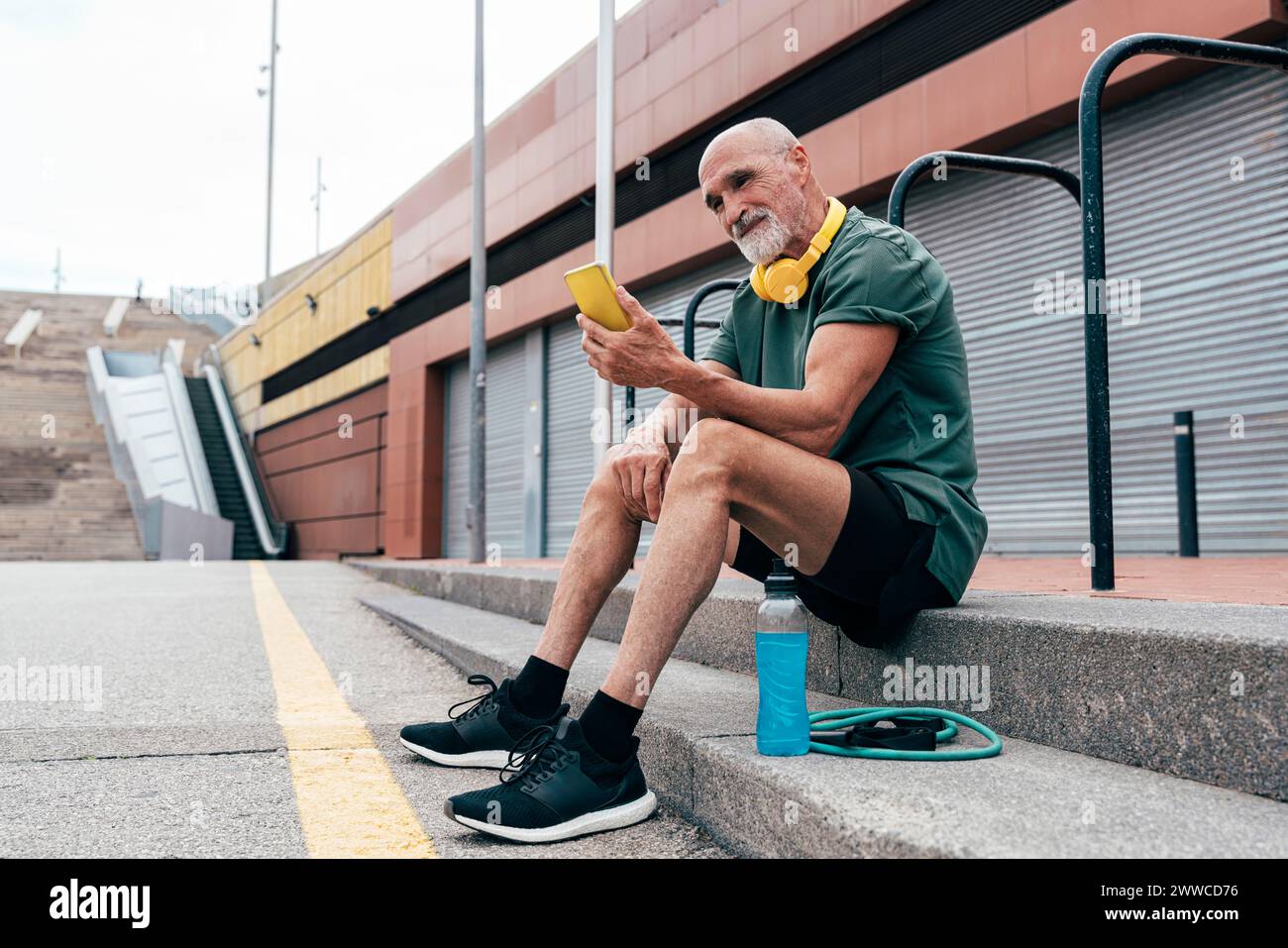 Smiling senior man using smart phone sitting on steps Stock Photo