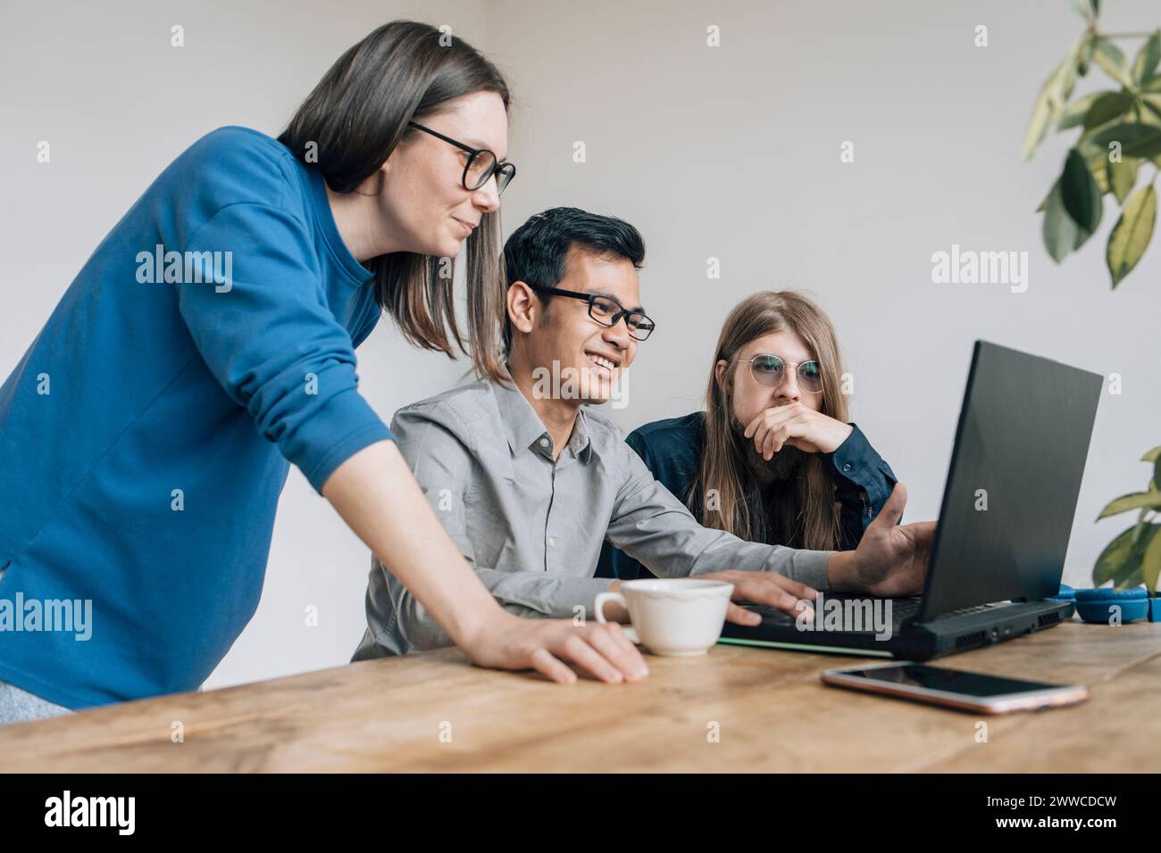 Smiling programmer discussing coding on laptop with colleagues at startup Stock Photo