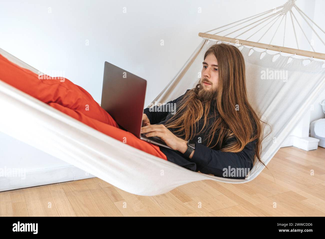 Young programmer on hammock using laptop for coding at startup in office Stock Photo