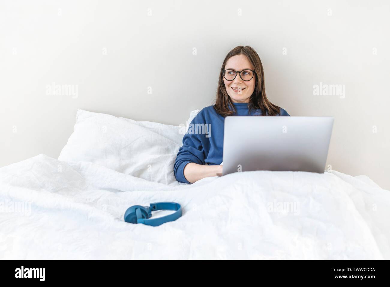 Smiling programmer using laptop sitting on bed at home Stock Photo