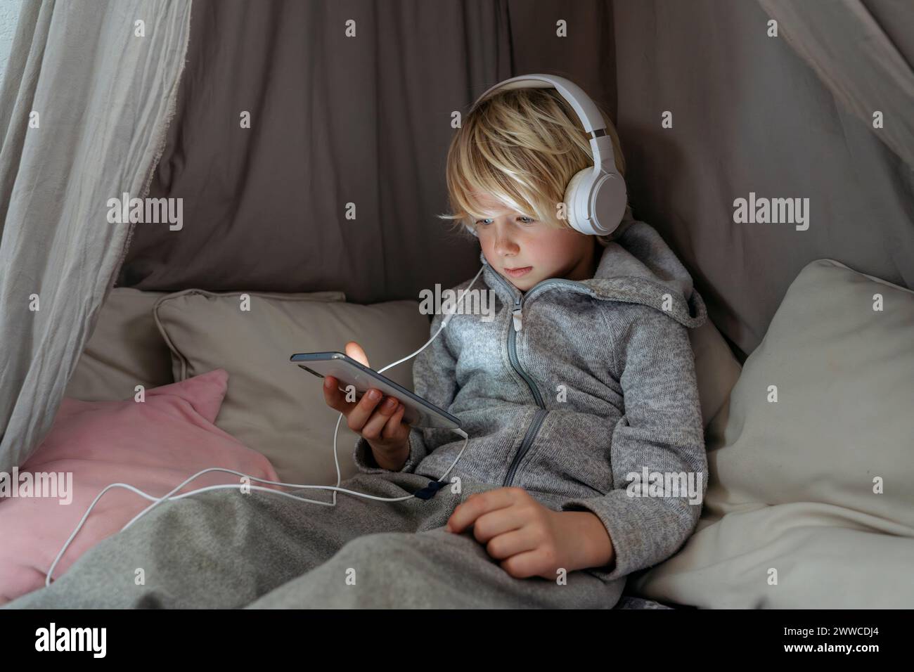 Boy wearing headphones using smart phone in canopy at home Stock Photo ...