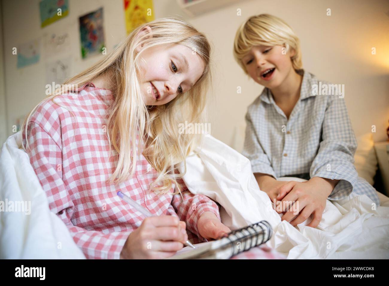 Girl drawing in book sitting with brother on bed at home Stock Photo