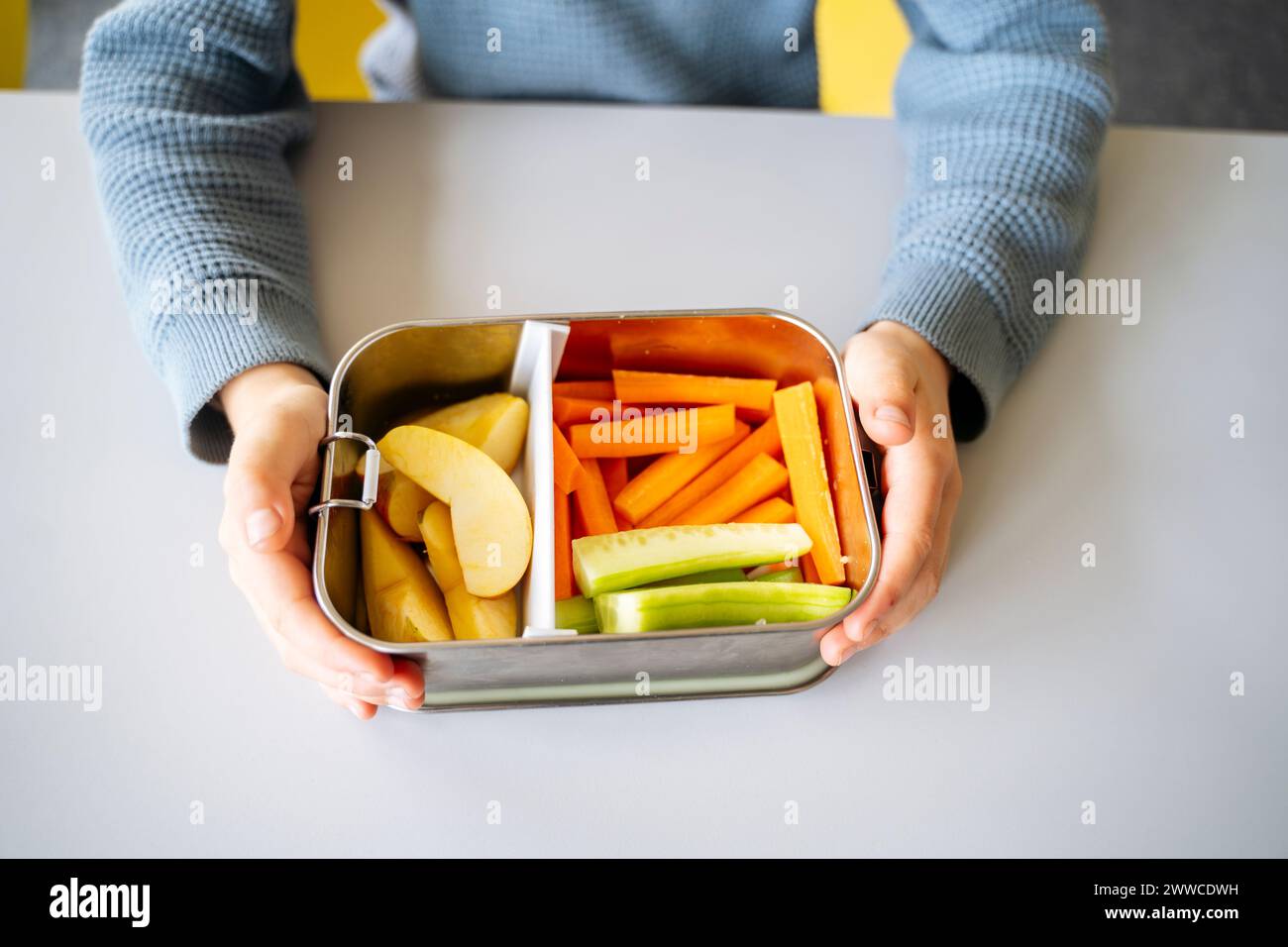 Hands of boy holding lunch box with fruits and vegetables at desk Stock Photo