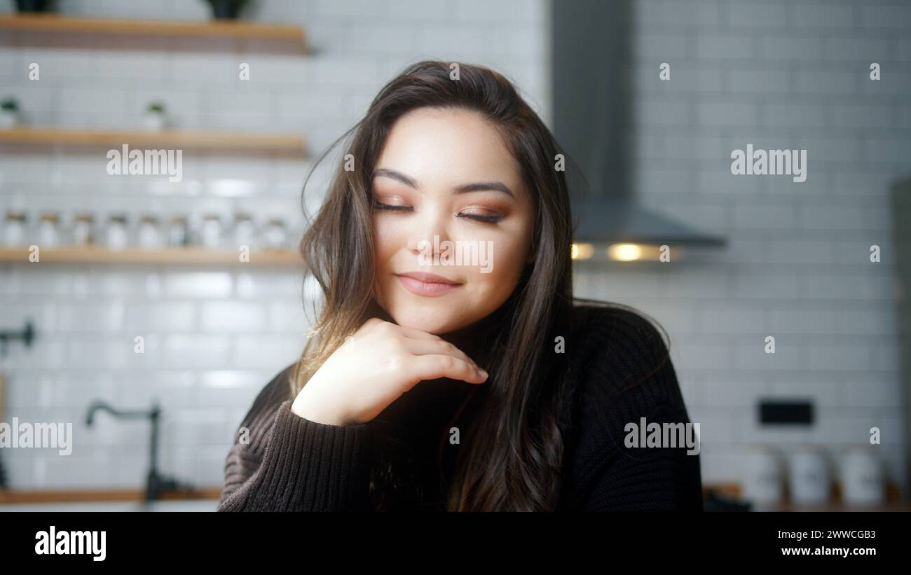 Portrait of closed eyes asian girl smiling in modern kitchen at home. Medium close-up Stock Photo