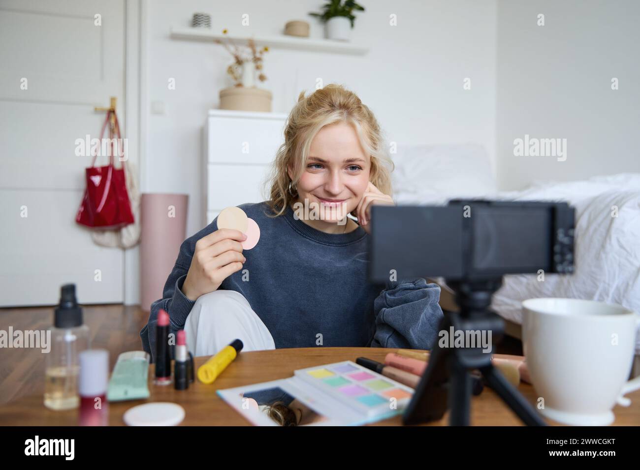 Image of young woman, vlogger records video on digital camera, shows beauty products, recommending makeup for audience on social media, sits on front Stock Photo