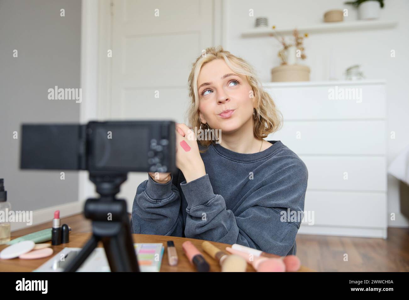 Portrait of young creative social media content creator, woman showing lipstick swatches on her hand, recording video about beauty and makeup, sitting Stock Photo