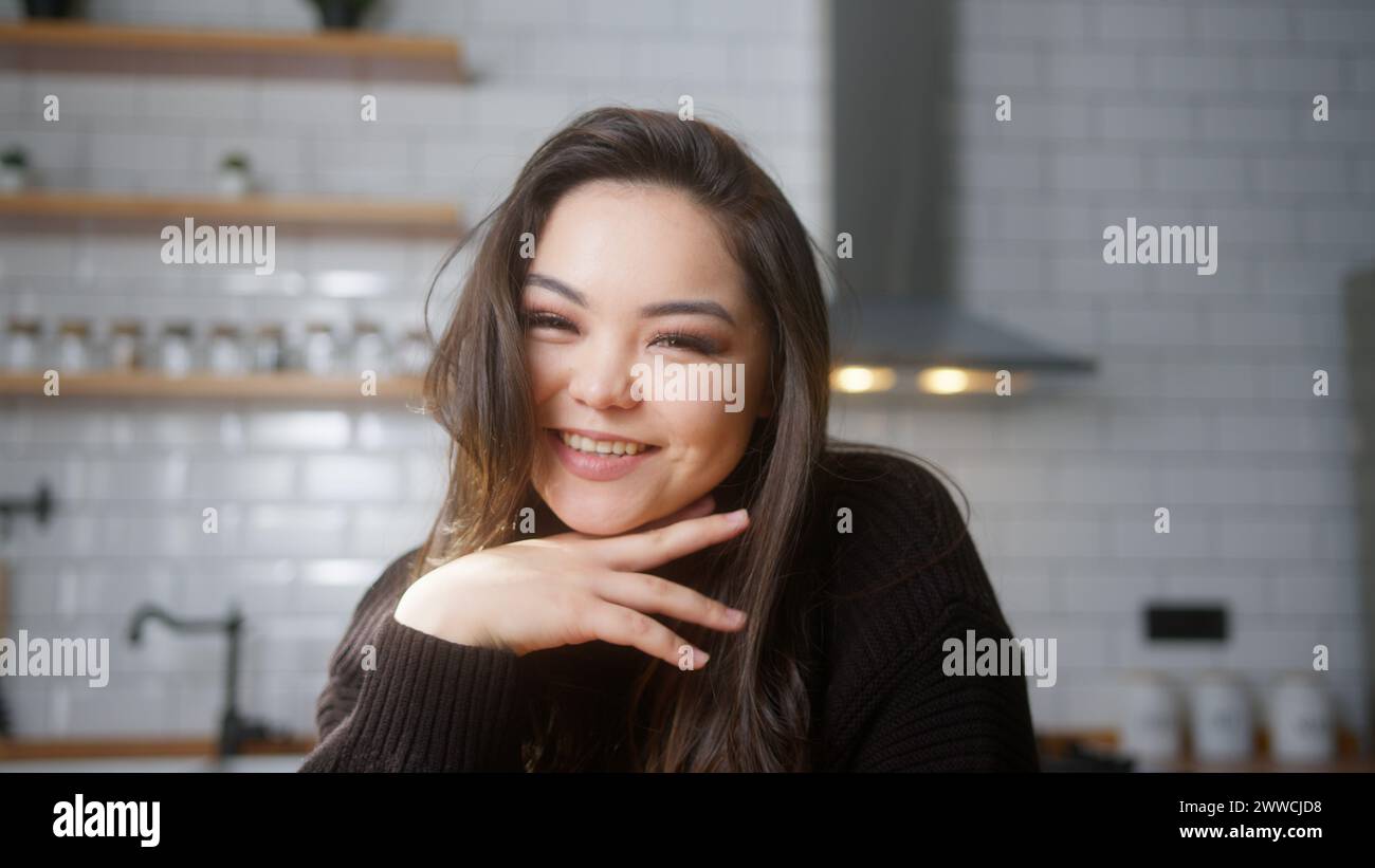 Portrait of beautiful asian woman looking at camera and smiling in modern kitchen at home. Medium close-up Stock Photo