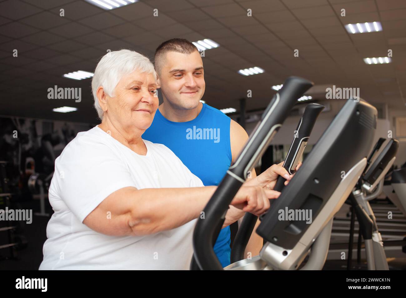 A coach and an elderly woman with gray hair in the gym. Exercise, weight loss, happy faces. Stock Photo