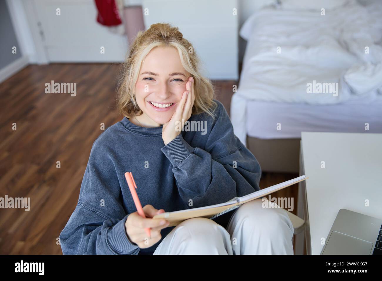 Portrait of smiling, charismatic young woman, writing down notes, making plans and putting it in planner, holding journal, sitting in bedroom and look Stock Photo
