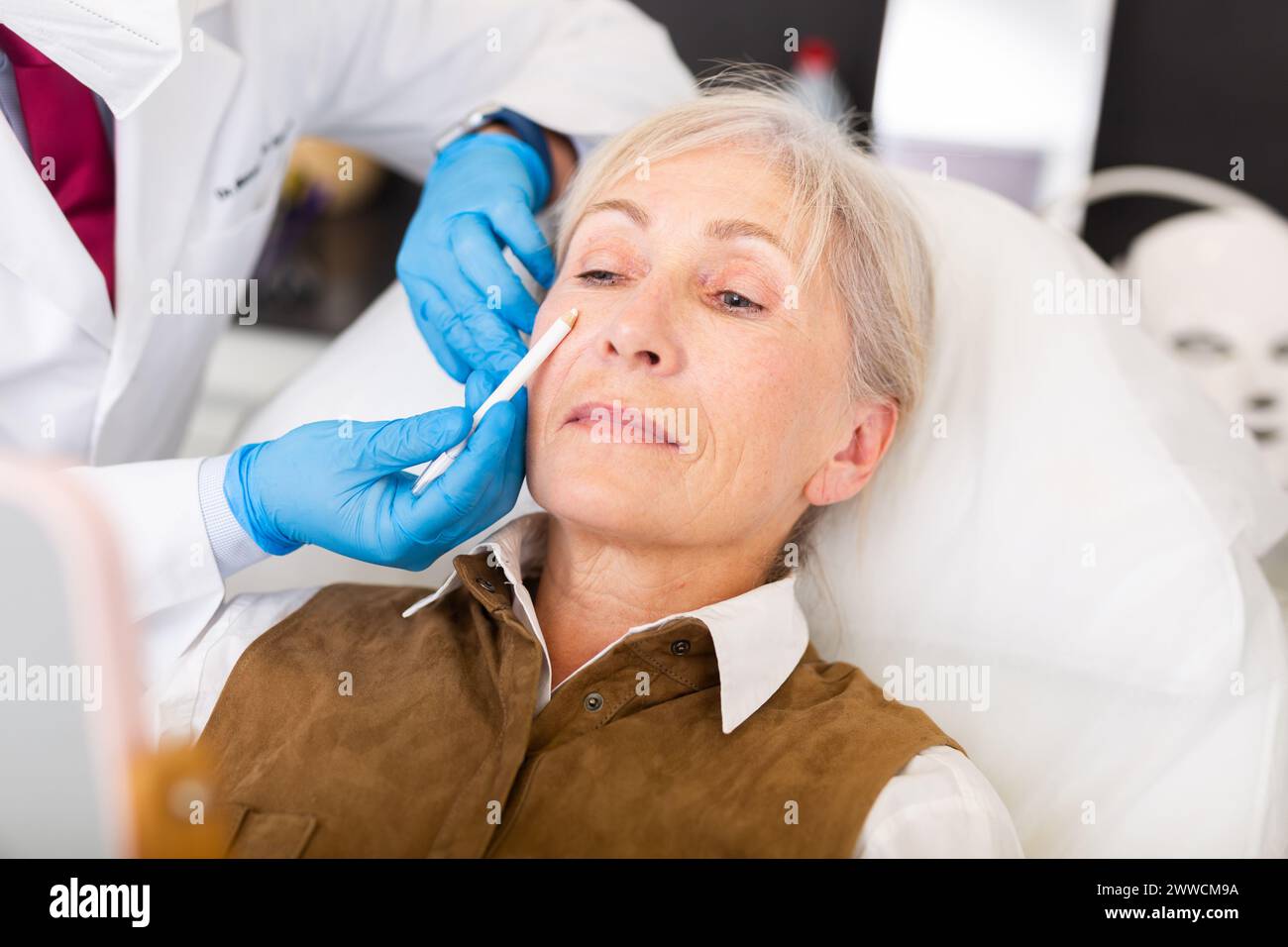 Plastic surgeon hands applying marks on face of elderly female patient Stock Photo