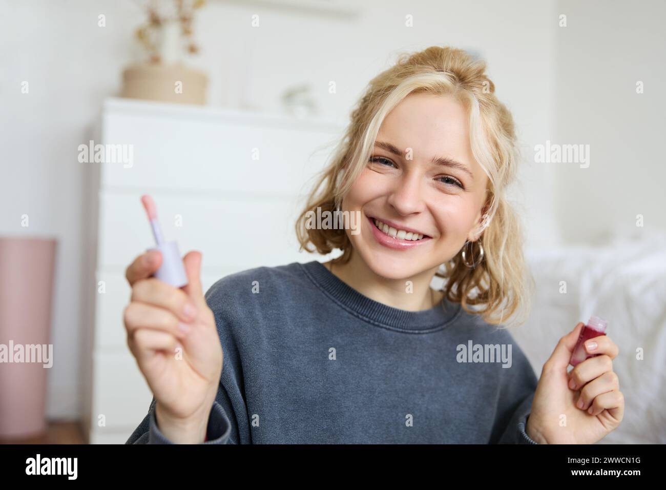 Close up portrait of woman recording a video of herself, holding beauty product, recommending lip gloss, content maker advertising makeup on her blog, Stock Photo