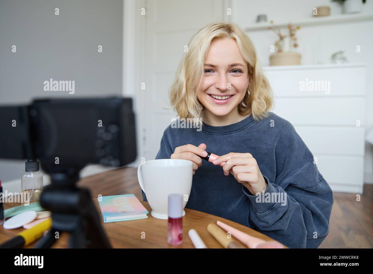 Portrait of beautiful, smiling blond woman, girl recording video of her makeup tutorial for social media, vlogger sitting on floor in her room, using Stock Photo