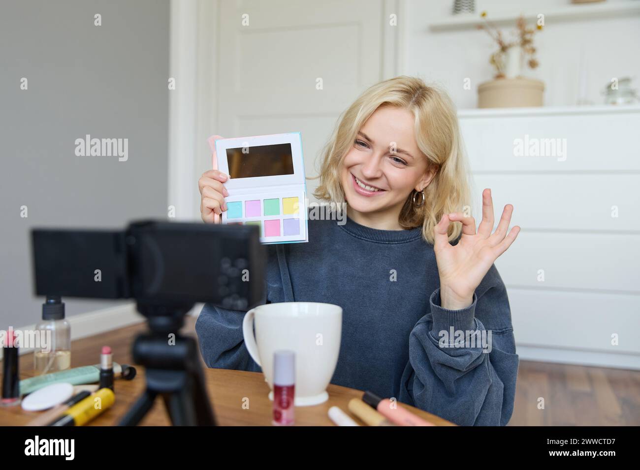 Portrait of beautiful smiling woman, recording video in her room, has camera on coffee table, reviewing makeup, doing lifestyle vlog for social media Stock Photo