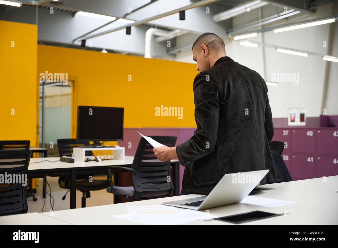 Young male manager leaning on table while reading paper document Stock Photo