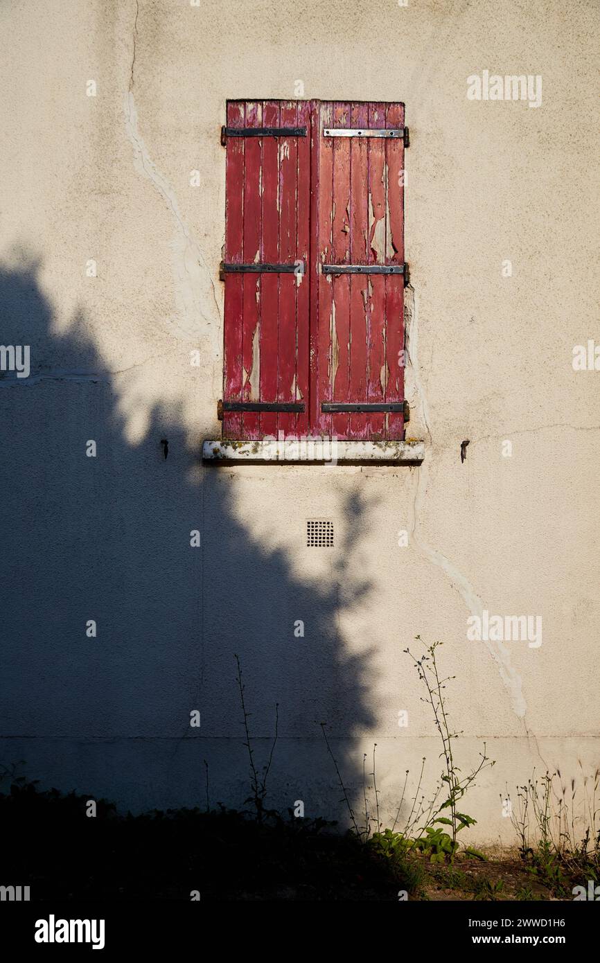 Peeling Red Paint on Window Shutter with Large Shadow on Wall Stock Photo