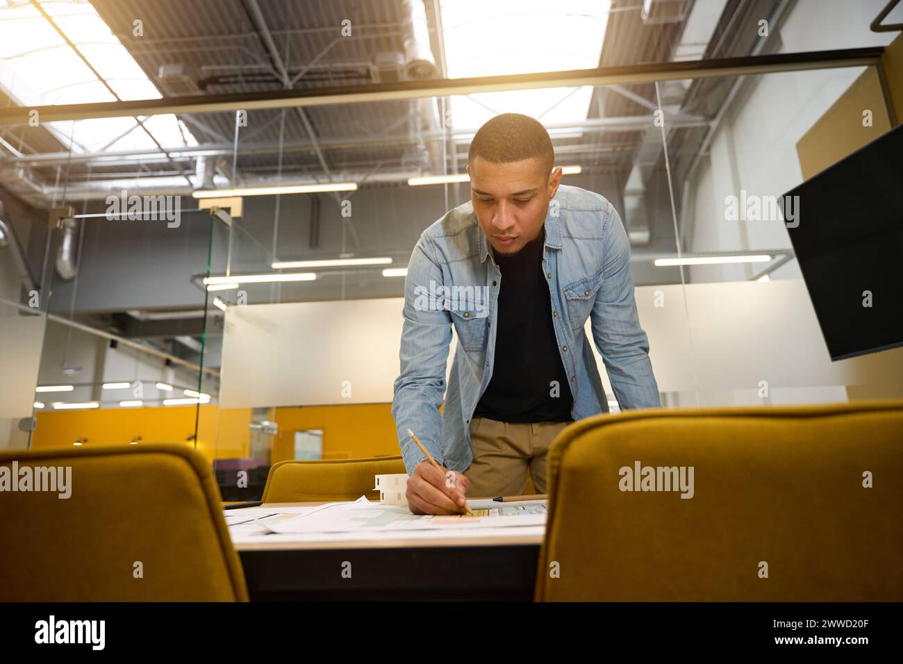 Serious young man leaning over table and writing something Stock Photo