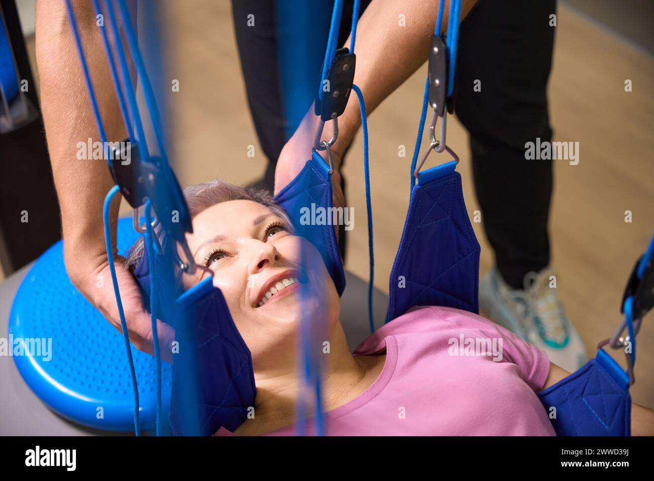 Cropped trainer helping smiling mature woman hanging on suspension ...
