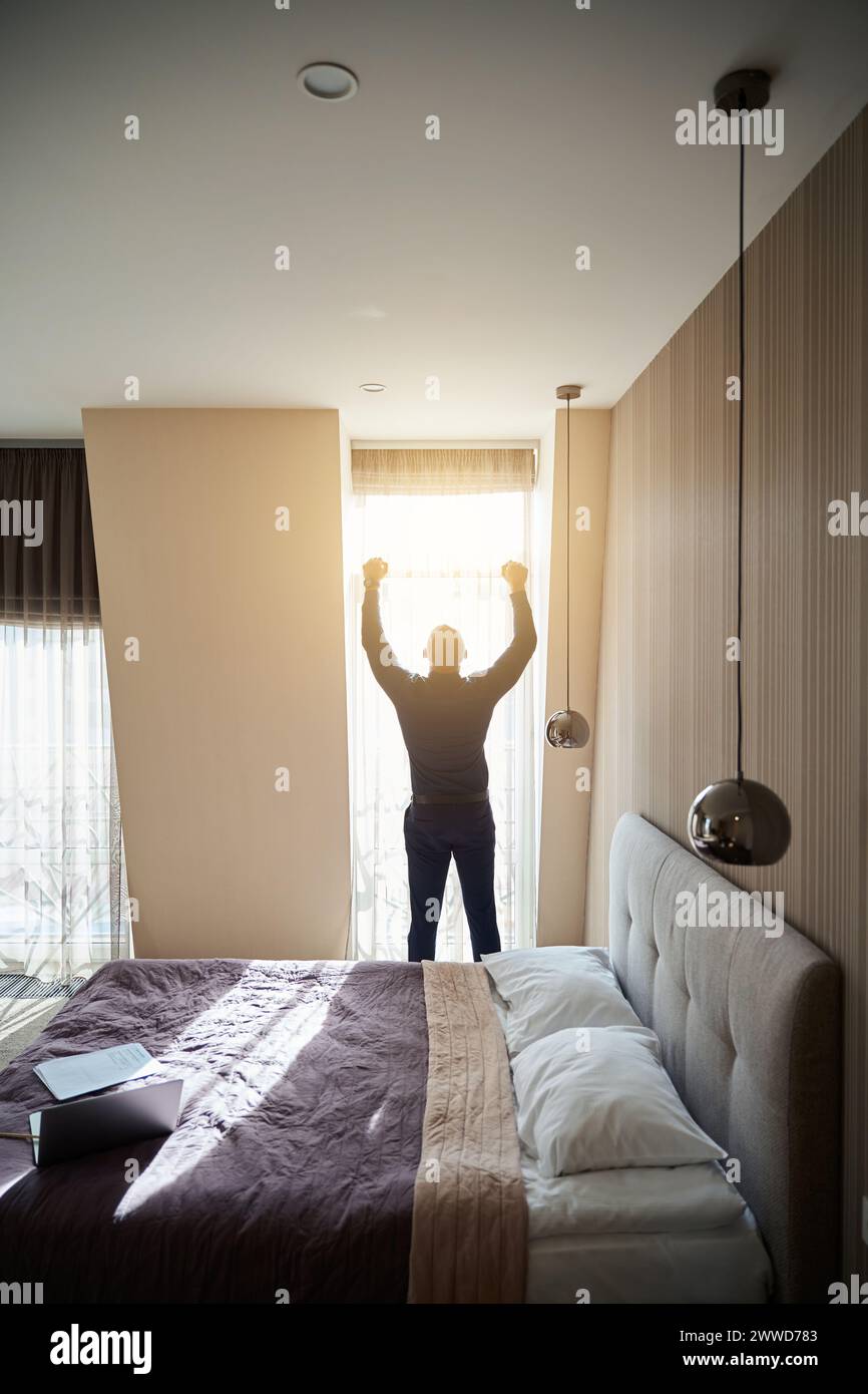 Back view of successful businessman with arms in air standing by window ...