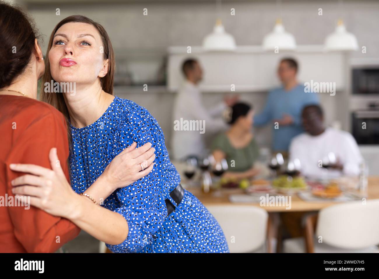 Hospitable hostess warmly greeting and kissing female friend Stock