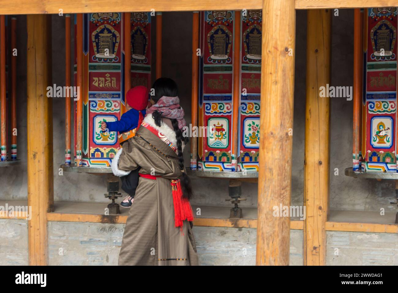 Mother and child in traditional clothes spinning the prayer wheels at the circuit around Labrang monastery, Xiahe County, Gansu province, China Stock Photo