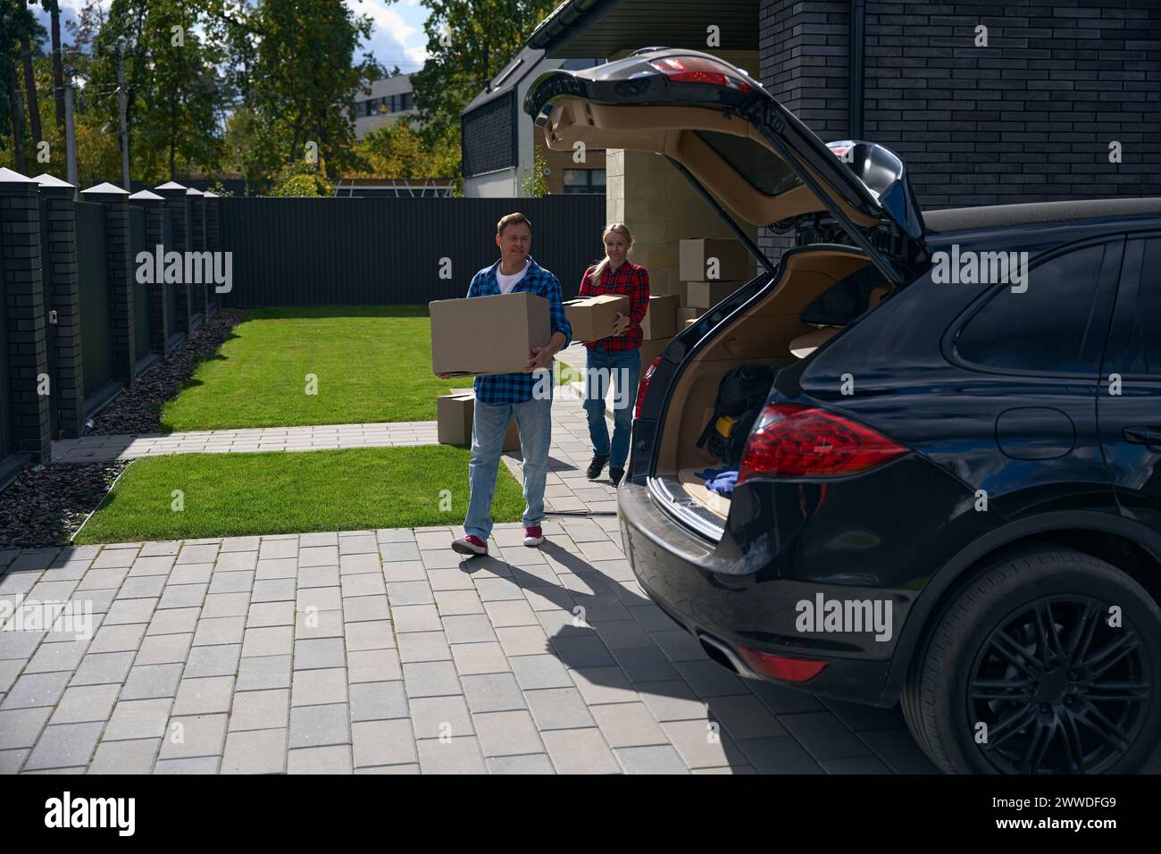 Cheerful couple carrying boxes to car during house move Stock Photo - Alamy