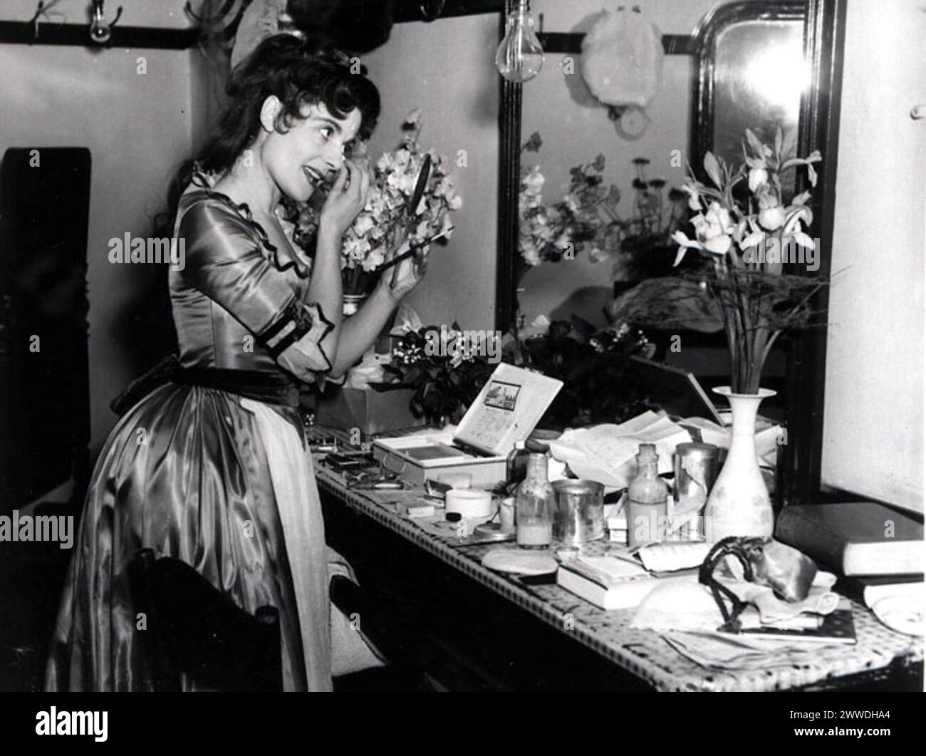 No business like it Description: Yvonne Mitchell in her dressing room at the Theatre Royal, Bath. The actress was touring with a production from Bristol Old Vic. Date: 22nd February 1949 flowers, woman, smile, standing, mirror, costume, bath, theatre, makeup, 1940s, dressingroom, actress, gown, backstage, 1949, bristololdvic, oldvic, yvonnemitchell, theatricalia:production=87t Stock Photo