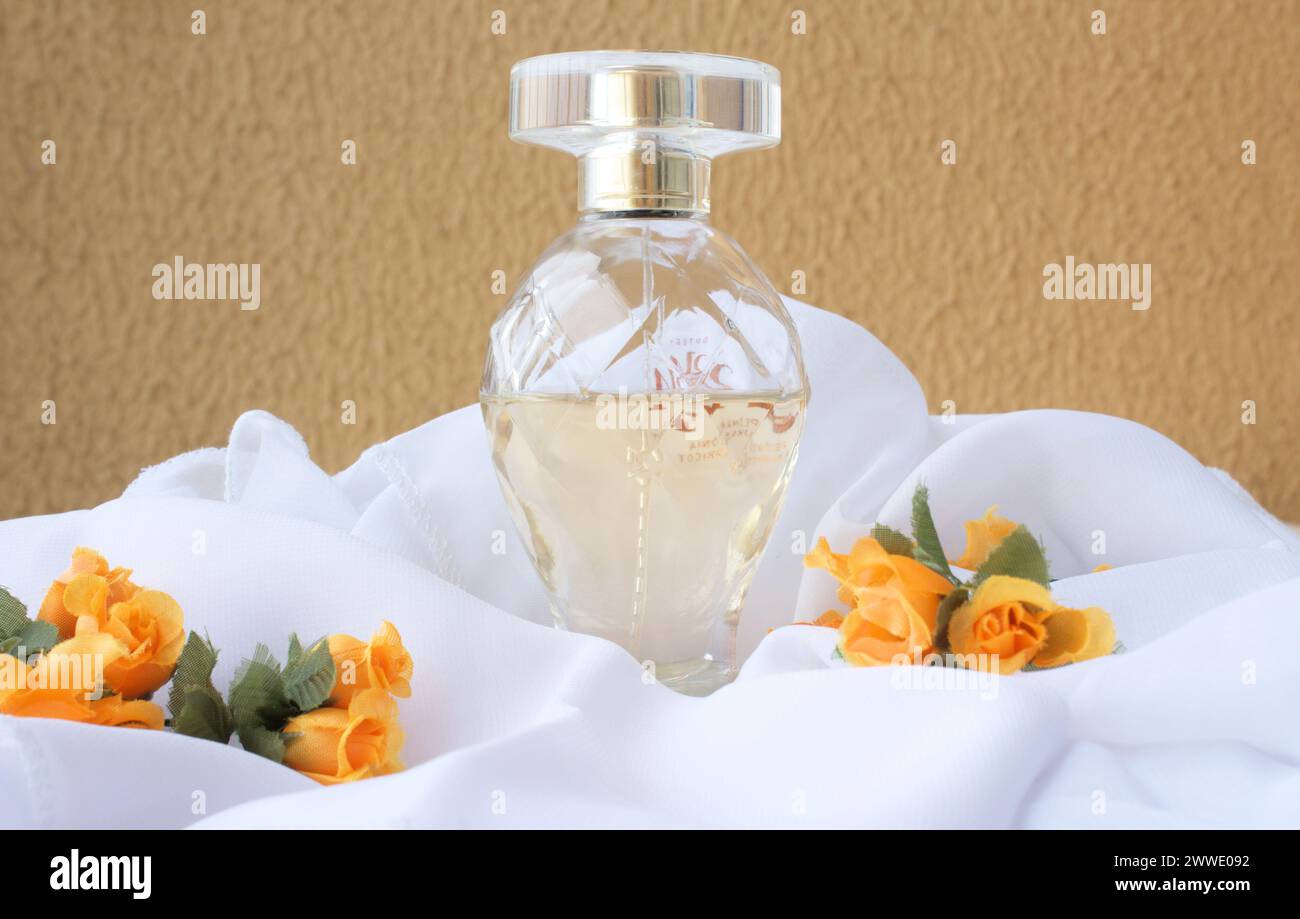 Female fragrance perfume on white fabric with orange color flowers in front of mustard color wall. Self care floral essence product. Eau de Parfum. Stock Photo