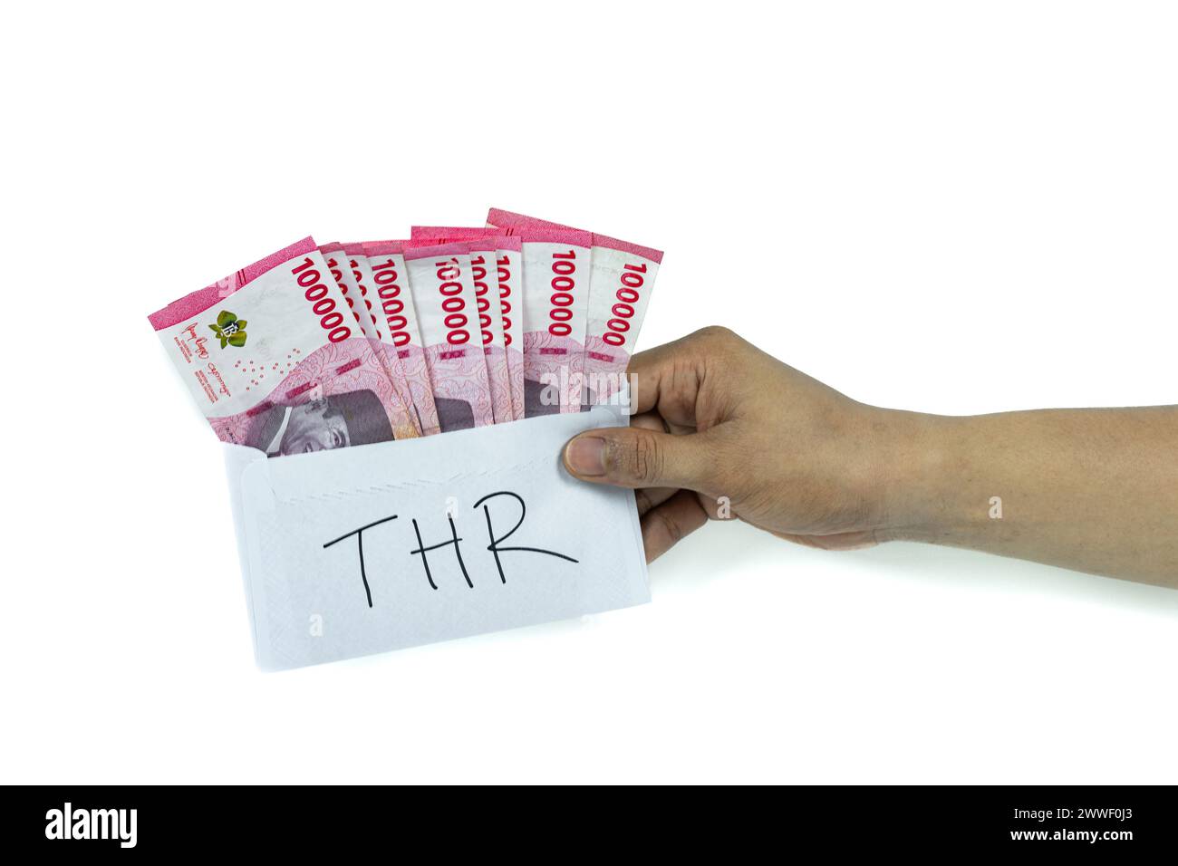 Asian man's hand holding white envelope with THR Text containing stack of IDR 100,000 cash.THR is holiday allowance on Eid al-Fitr or Lebaran days. Stock Photo