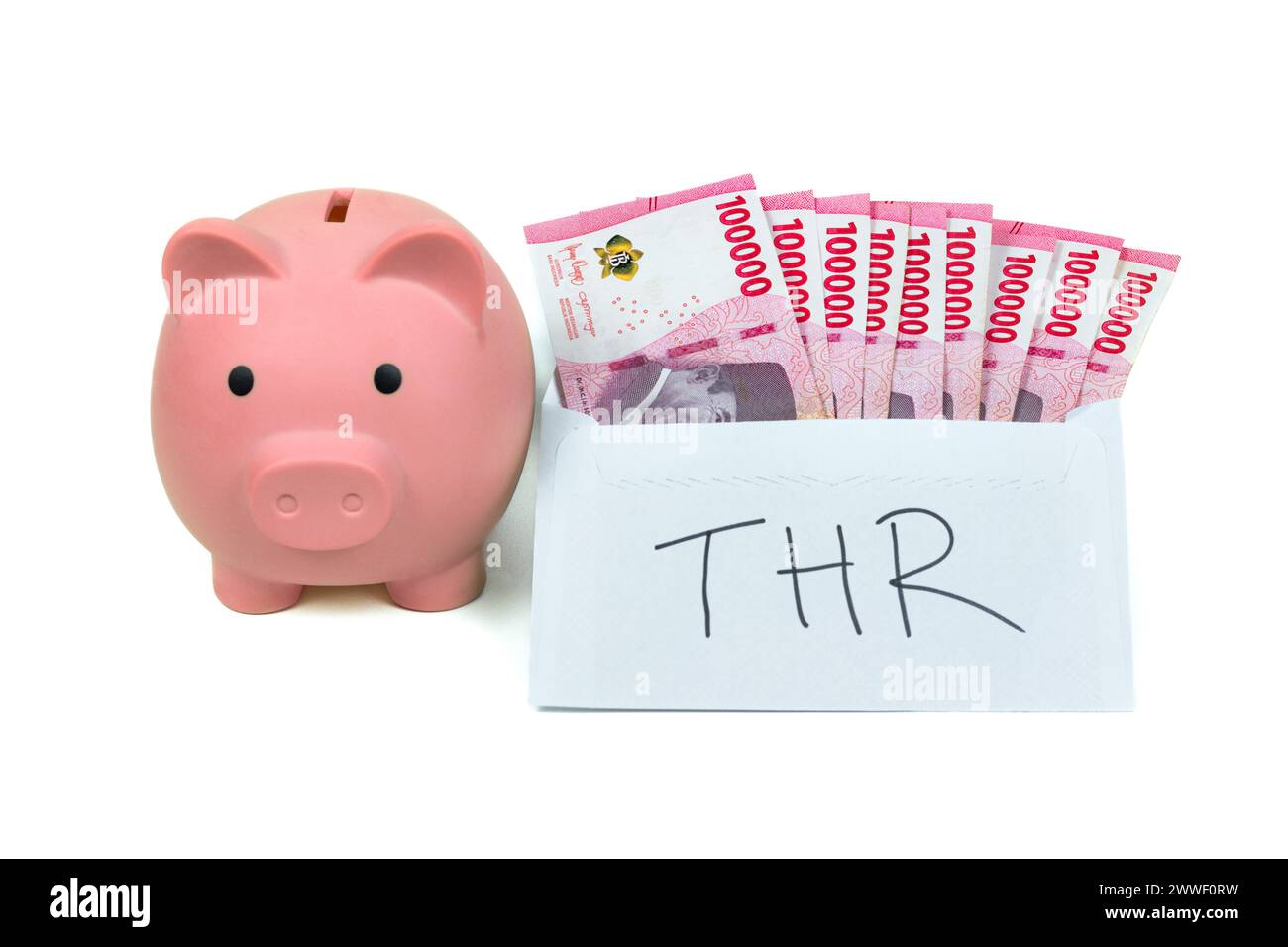 Piggy bank with stack of Rupiah or IDR banknotes inside white envelope with THR Text. THR is holiday allowance on Eid al-Fitr or Lebaran days. Stock Photo