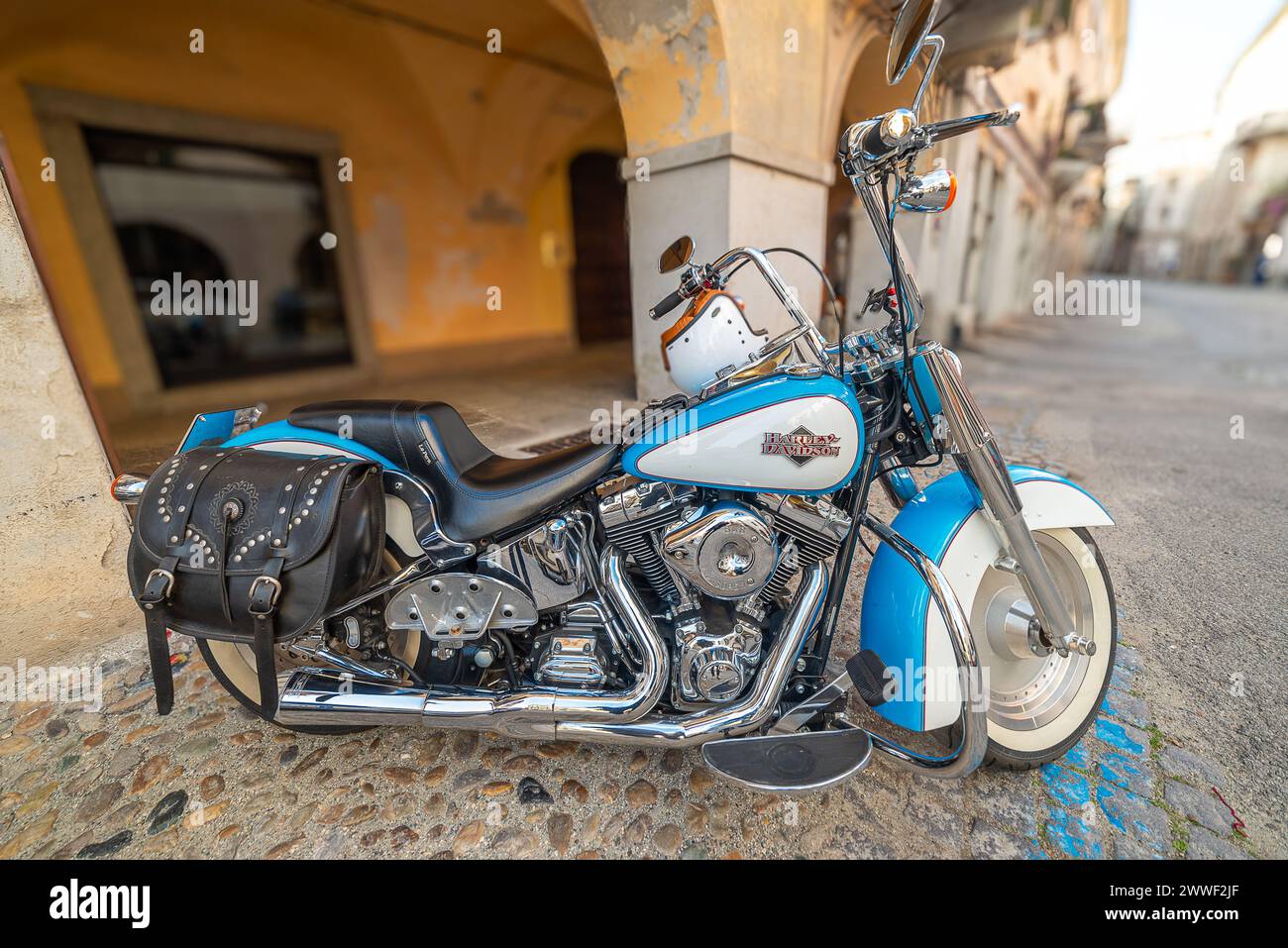 Savigliano, Cuneo, Italy - March 21, 2024: Harley Davidson custom motorcycle parked on cobblestones of historic downtown street Stock Photo