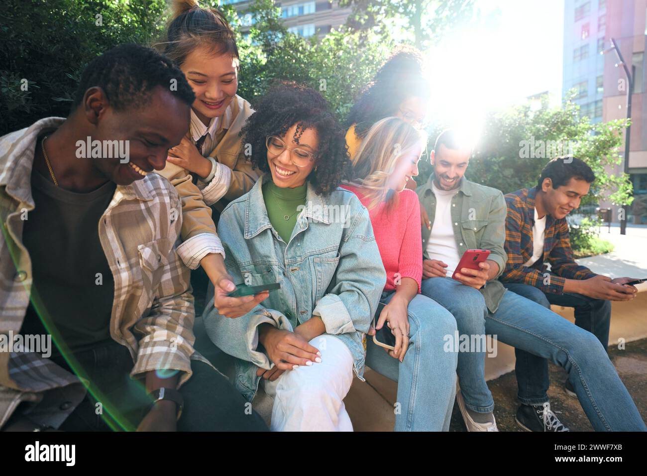 Diverse group university friends sitting on stairs in street city. Happy students using smartphones. Stock Photo