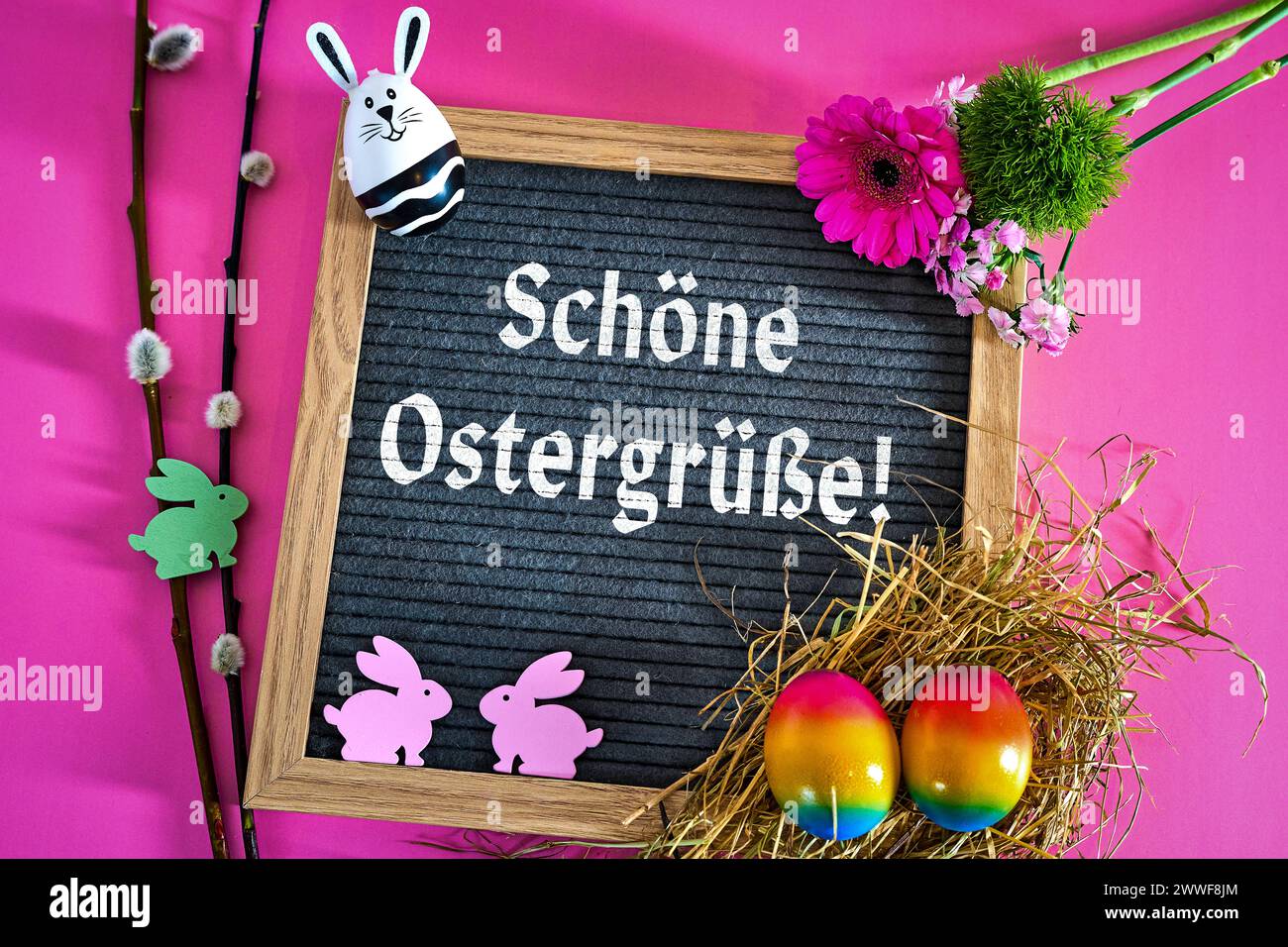 Augsburg, Bavaria, Germany - March 23, 2024: Happy Easter greetings Lettering on a blackboard surrounded by Easter decoration with Easter nest and colorful eggs. PHOTOMONTAGE *** Schöne Ostergrüße Schriftzug auf einer Tafel umgeben von Osterdekoration mit Osternest und bunten Eiern. FOTOMONTAGE Stock Photo