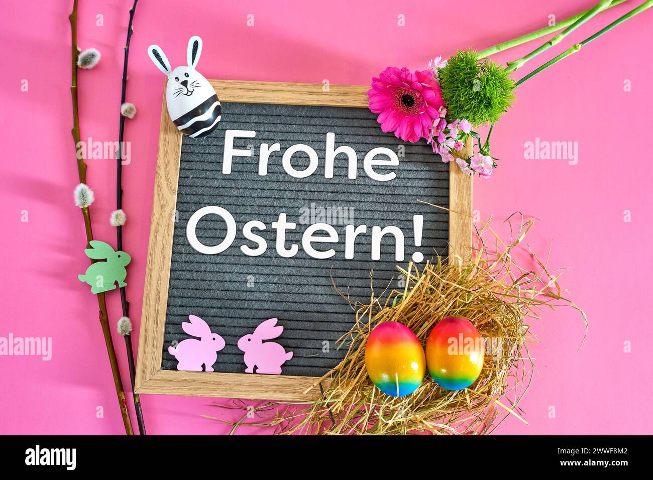 Augsburg, Bavaria, Germany - March 23, 2024: Plaque with greeting: Happy Easter Decorated with an Easter nest made of straw and colorful eggs and small Easter bunny figures. PHOTOMONTAGE *** Tafel mit Gruß: Frohe Ostern Dekoriert mit Osternest aus Stroh und bunten Eiern und kleinen Osterhasen Figuren. FOTOMONTAGE Stock Photo