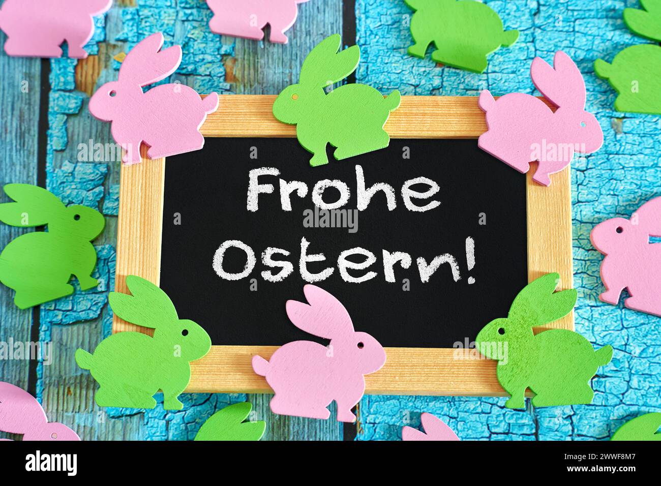 Augsburg, Bavaria, Germany - March 23, 2024: Greetings for Easter: Happy Easter Lettering on a board with lots of colorful little wooden Easter bunnies. PHOTOMONTAGE *** Grüße zu Ostern: Frohe Ostern Schriftzug auf einer Tafel mit vielen bunten kleinen Osterhasen aus Holz. FOTOMONTAGE Stock Photo