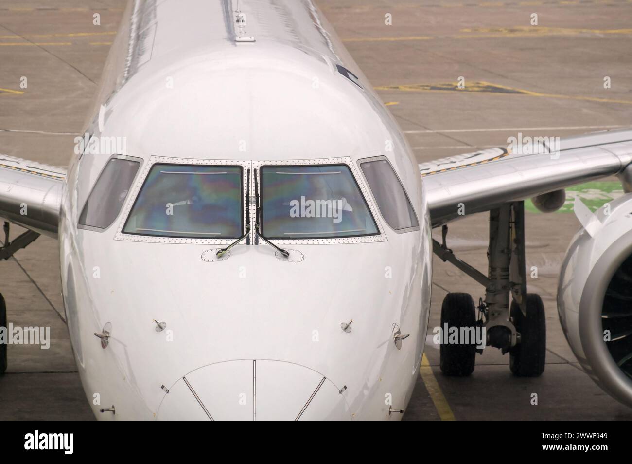 Front view of white modern jet airliner with close-up of cockpit windows. The plane is sitting on a concrete tarmac with painted lane lines Stock Photo