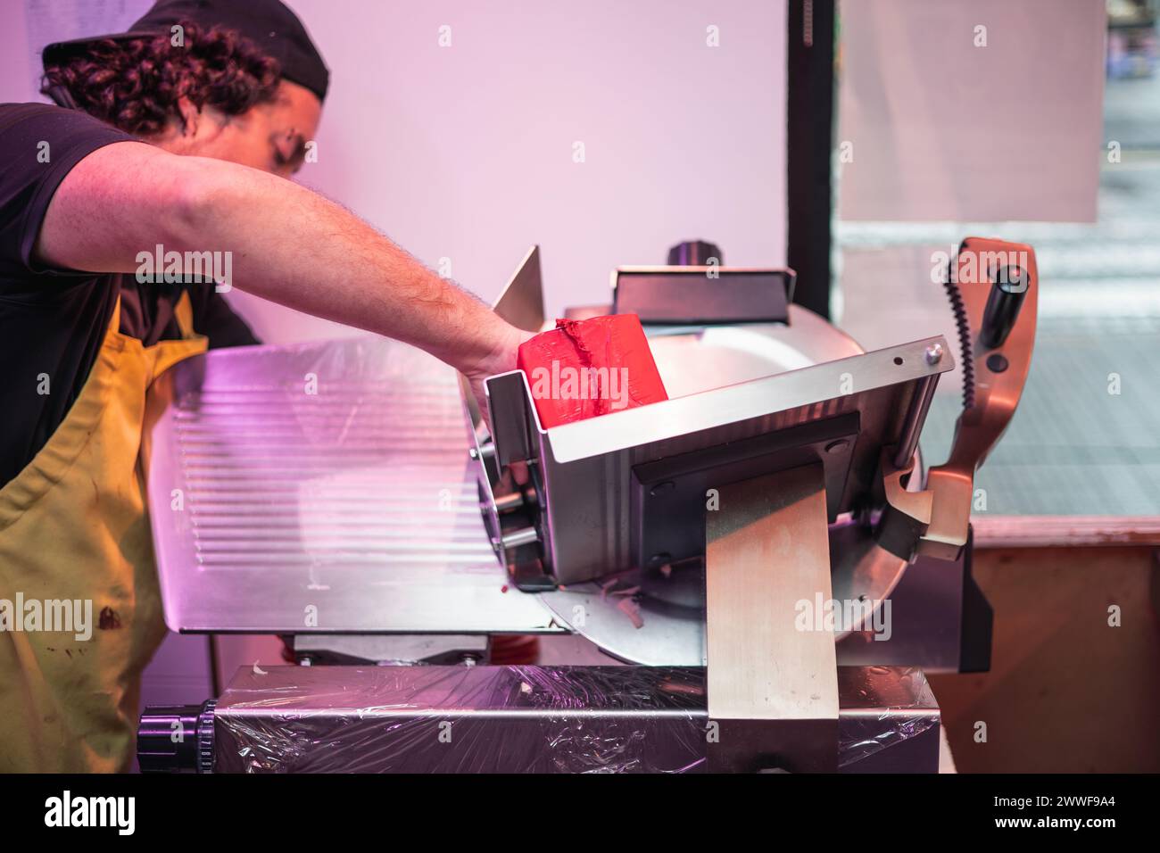 closeupbutcher slicing pork loin using an electric slicer in his butcher shop. The scene showcases the efficiency and precision of meat preparation in Stock Photo