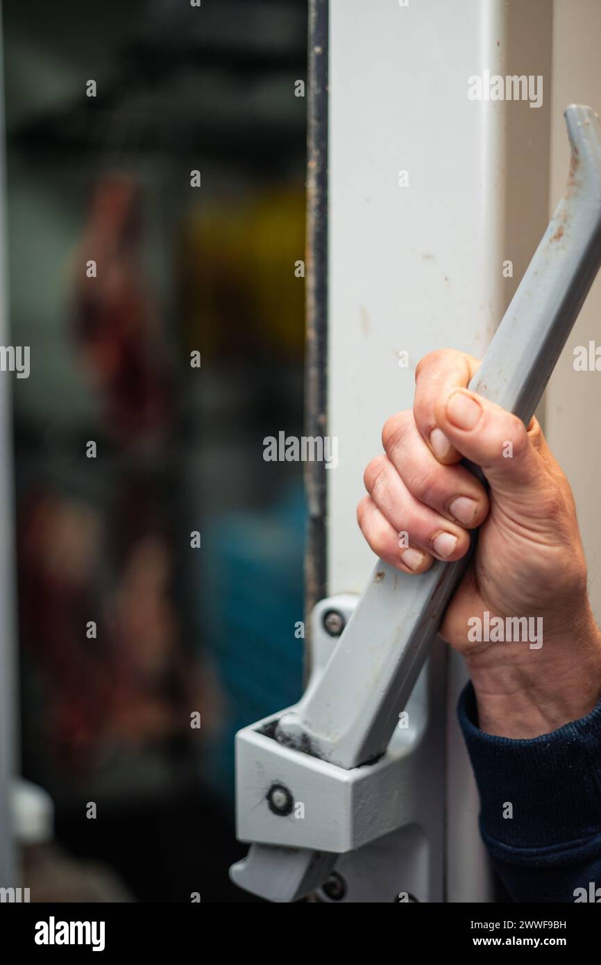 vertical portrait closeup of a hand opening a refrigerated meat storage unit. The scene emphasizes the significance of refrigerated storage in maintai Stock Photo