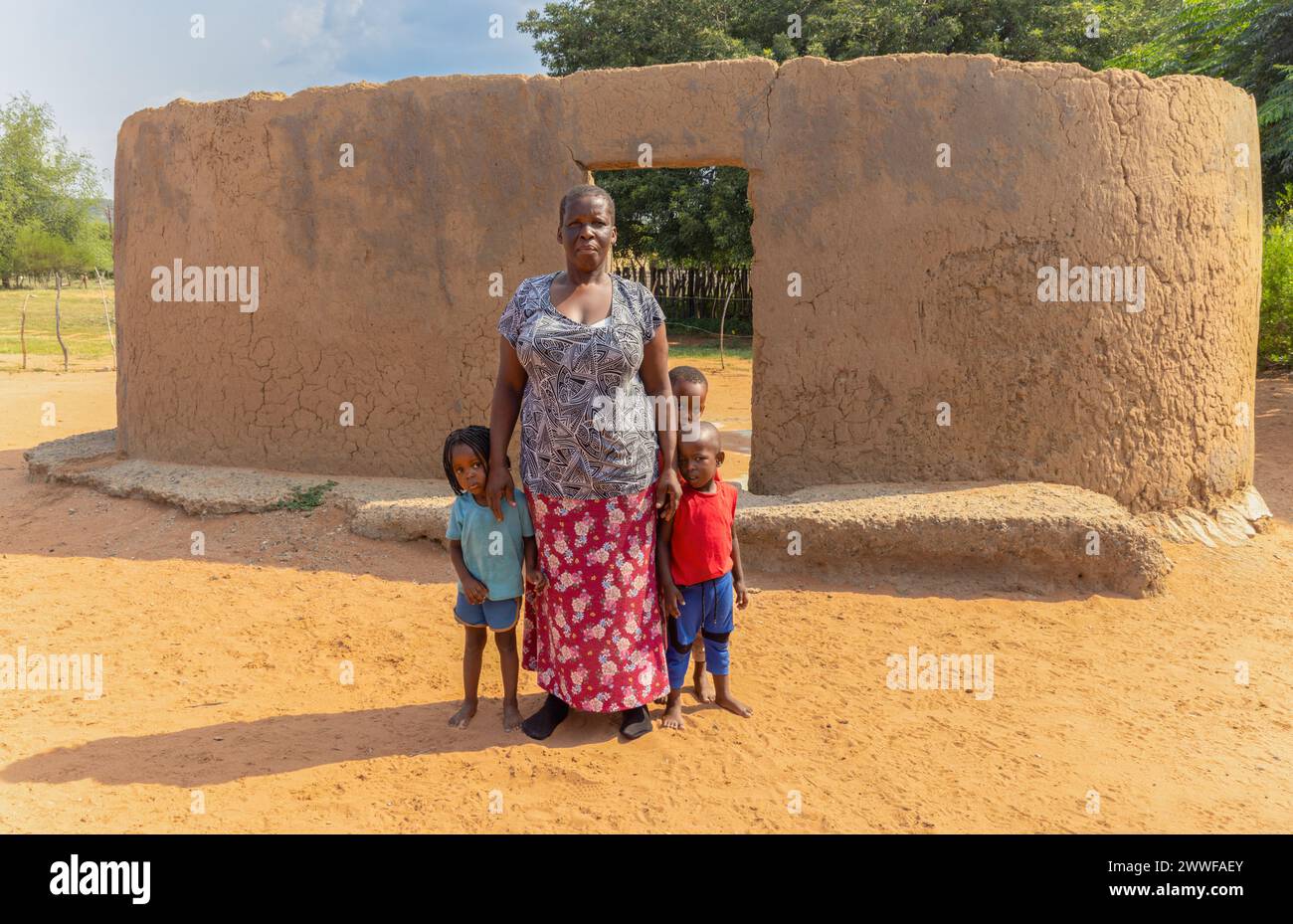 village african mother with three kids standing in front of a ruined mud house in the village Stock Photo