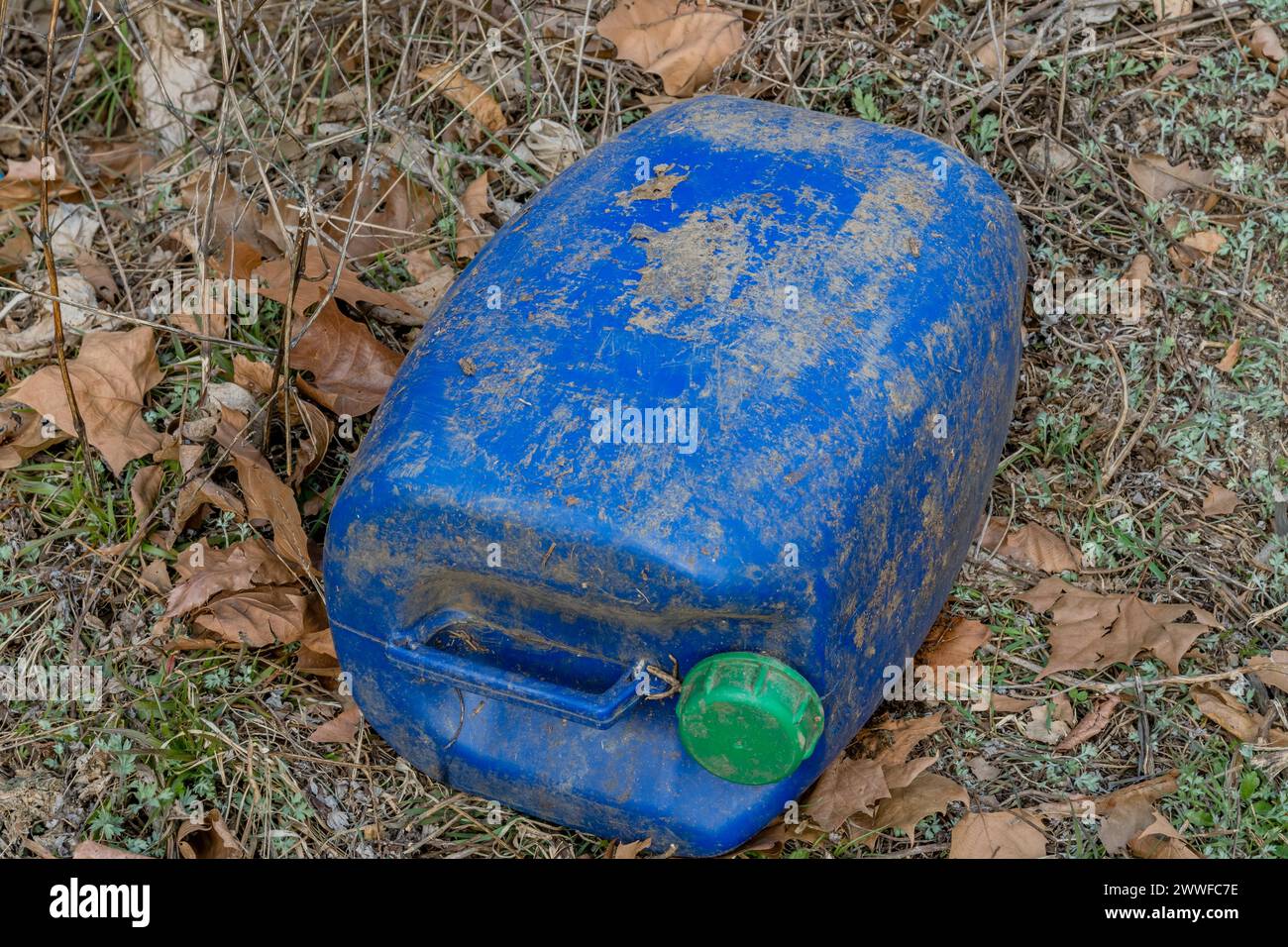 Weathered blue plastic barrel with a green cap surrounded by leaves, in