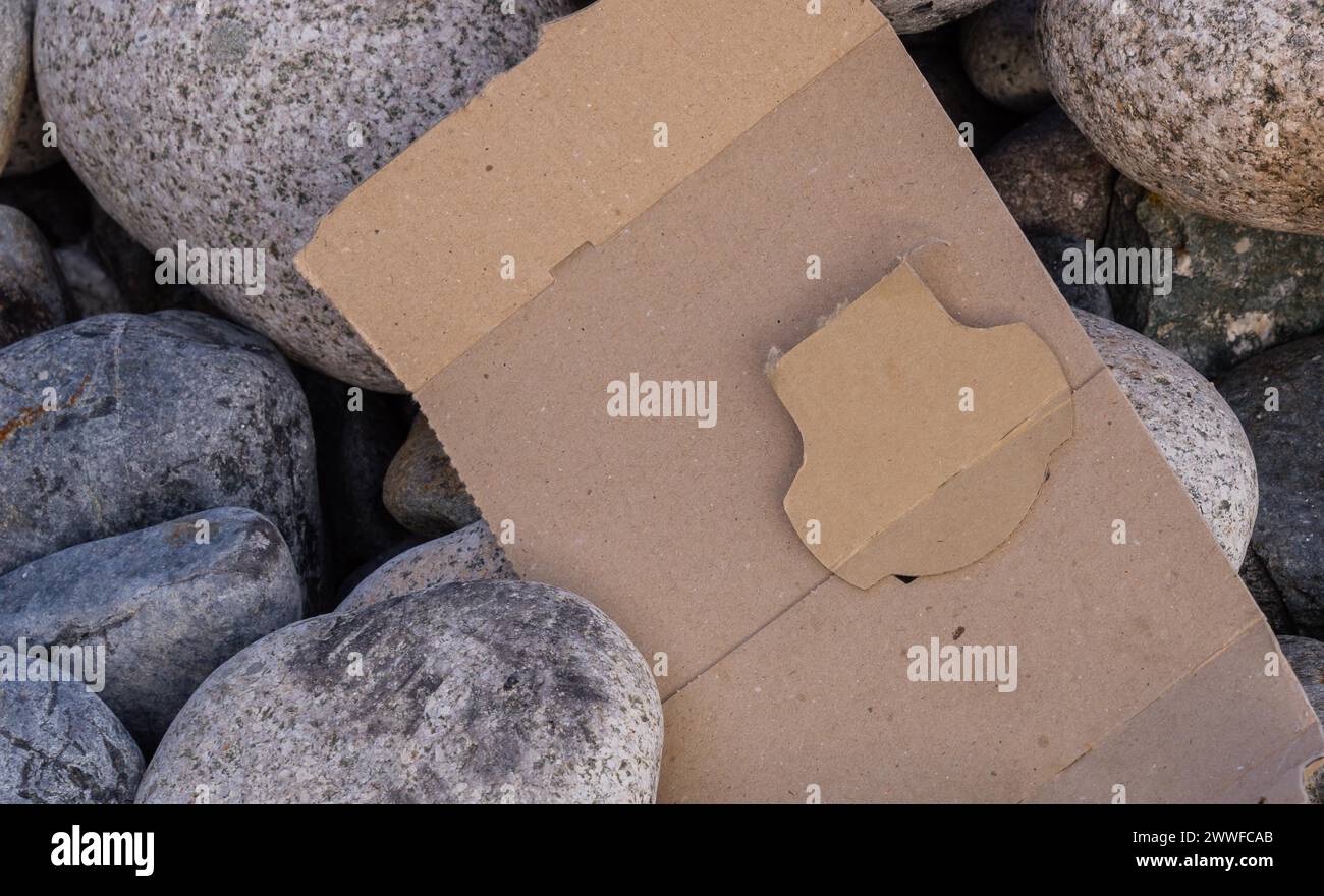 A plain cardboard shape surrounded by stones, hinting at environmental disregard, in South Korea Stock Photo